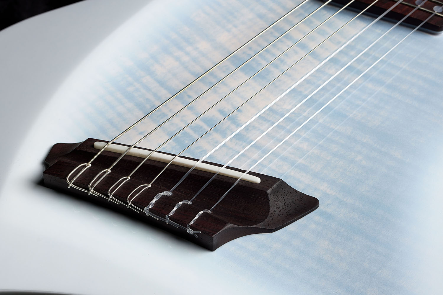 Close-up of the Abasi Stage 7 White Burst's rosewood bridge and bone saddle, showing the flame maple top's figured grain and blue-white burst coloring.