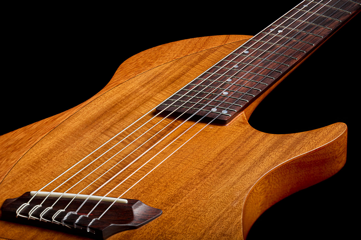 Close-up of the Abasi Stage 7 Acacia's rosewood bridge and bone saddle, with strings anchored through the acacia-veneer top.