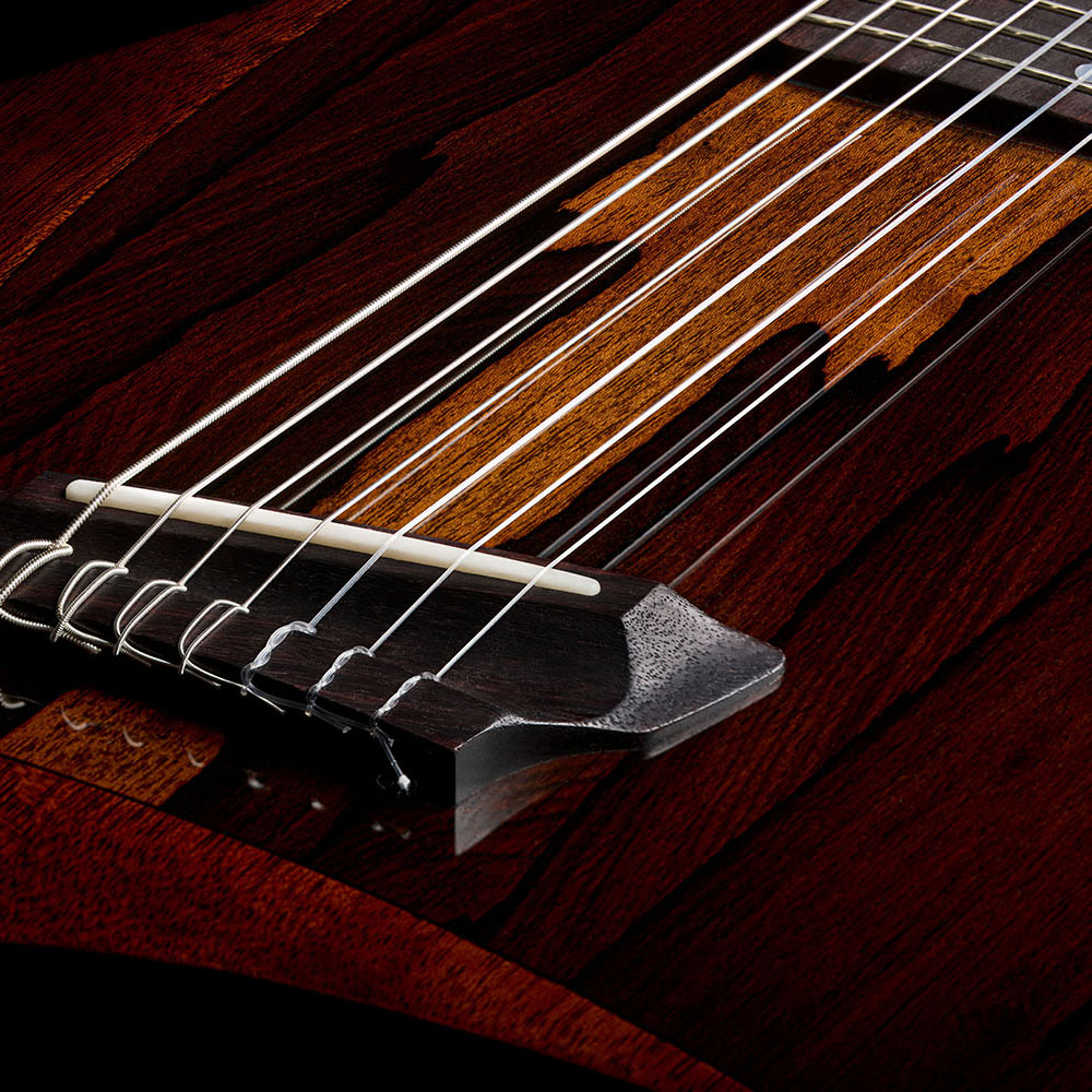 Close-up of the Abasi Stage 7 Ziricote's rosewood bridge and bone saddle, showing the ziricote top veneer's dark streaked grain.