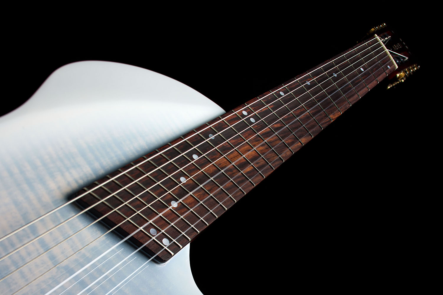 Close-up of the Abasi Stage 7 White Burst's fanned frets and dot inlays, with the white burst body curve blurred in the background.