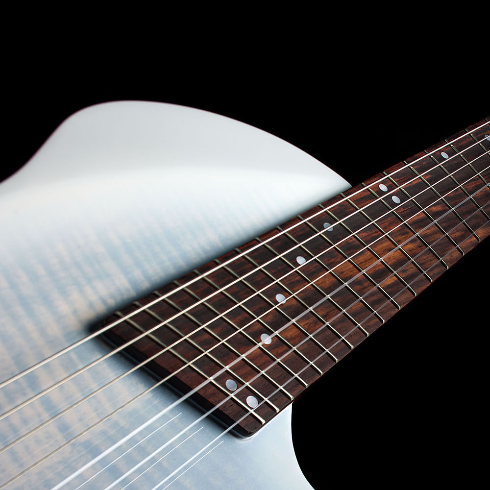 Close-up of the Abasi Stage 7 White Burst's fanned frets and dot inlays, with the white burst body curve blurred in the background.