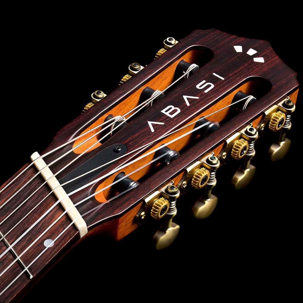 Close-up of the Abasi Stage 7 Acacia's fanned headstock, showing the inlaid ABASI logo and brass tuning machines.
