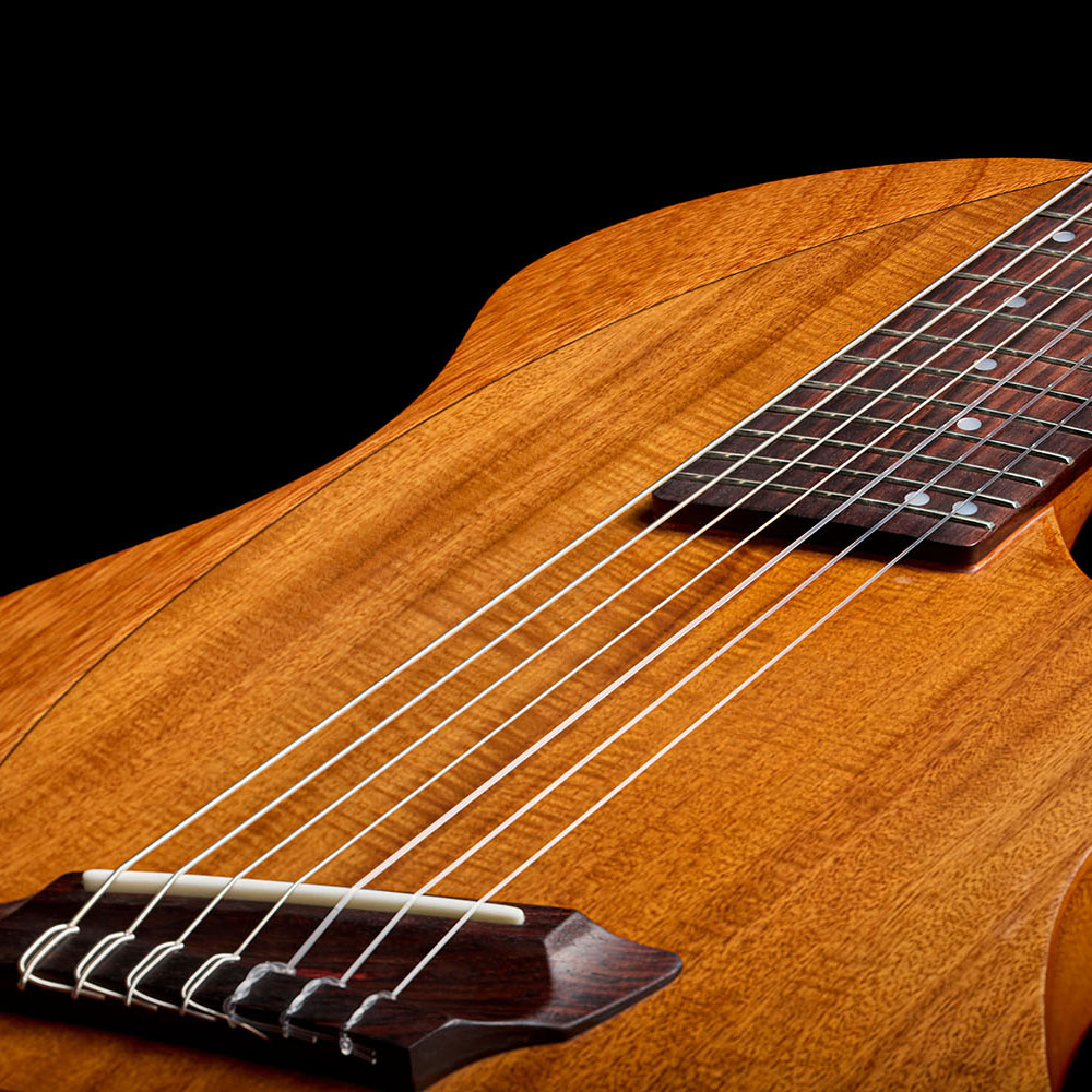 Close-up of the Abasi Stage 7 Acacia's rosewood bridge and bone saddle, with strings anchored through the acacia-veneer top.