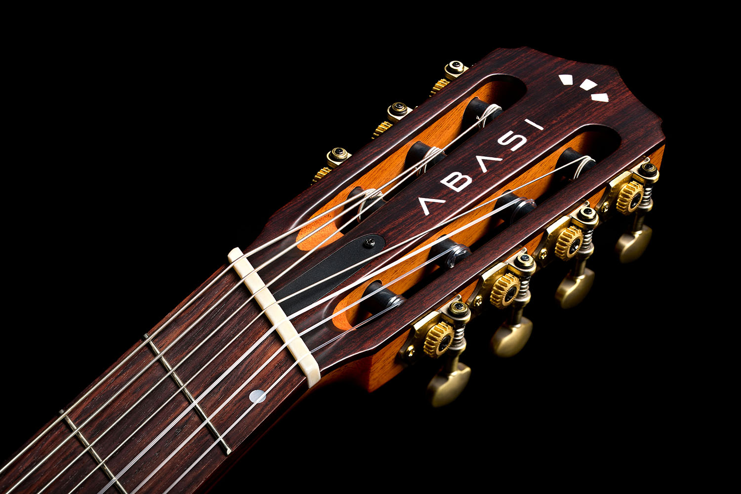 Close-up of the Abasi Stage 7 Acacia's fanned headstock, showing the inlaid ABASI logo and brass tuning machines.